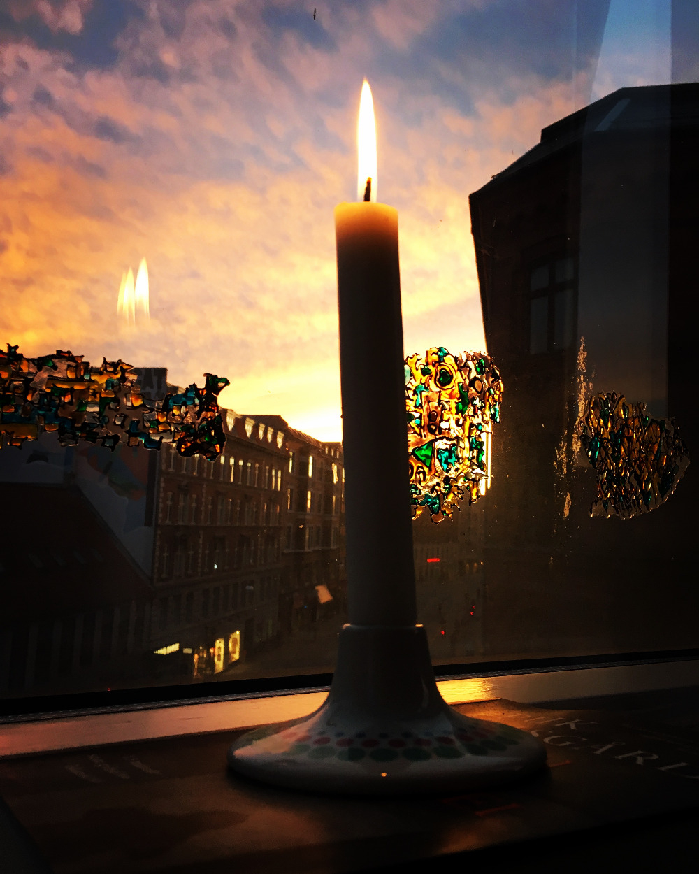 Stearinlys i vindueskarm med udsigt til huse, gade og solnedgang